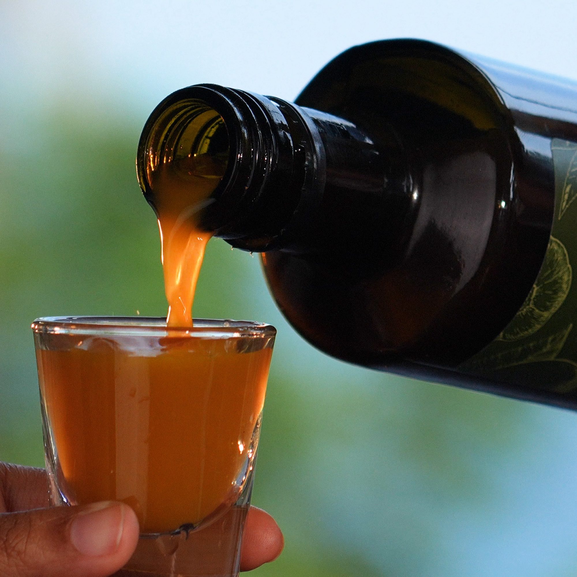 Natural Elixir CBD infused tonic being poured from the bottle into a glass shot glass