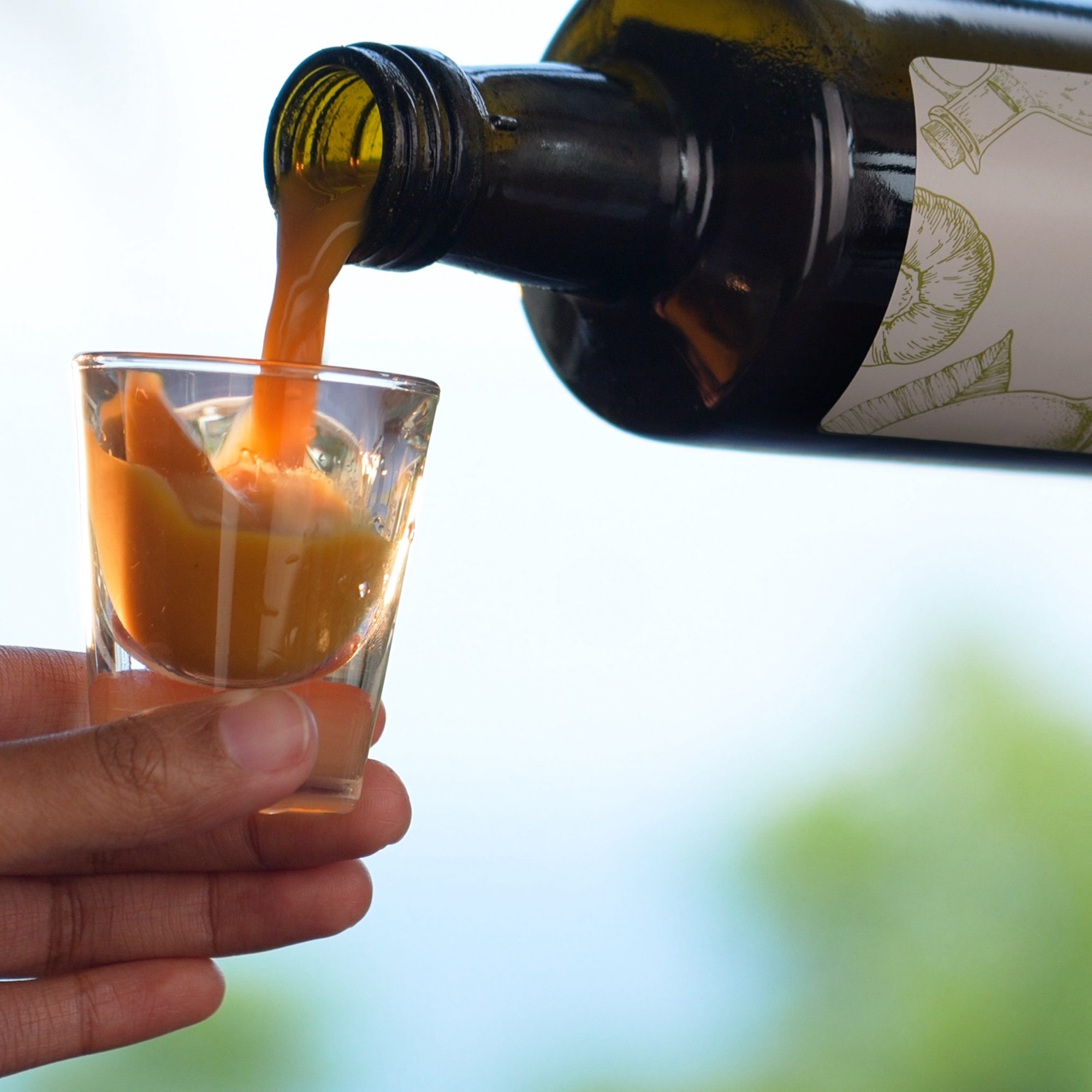 Natural Elixir Classic tonic being poured from the bottle into a glass shot glass