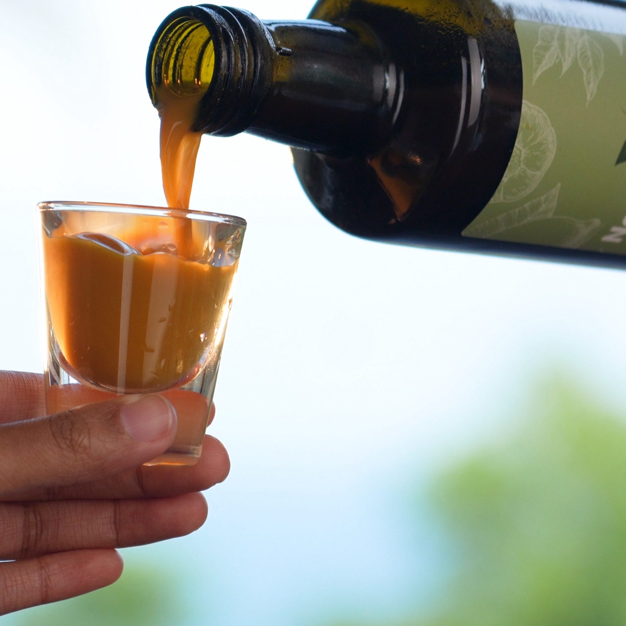 Natural Elixir LITE tonic being poured from the bottle into a glass shot glass