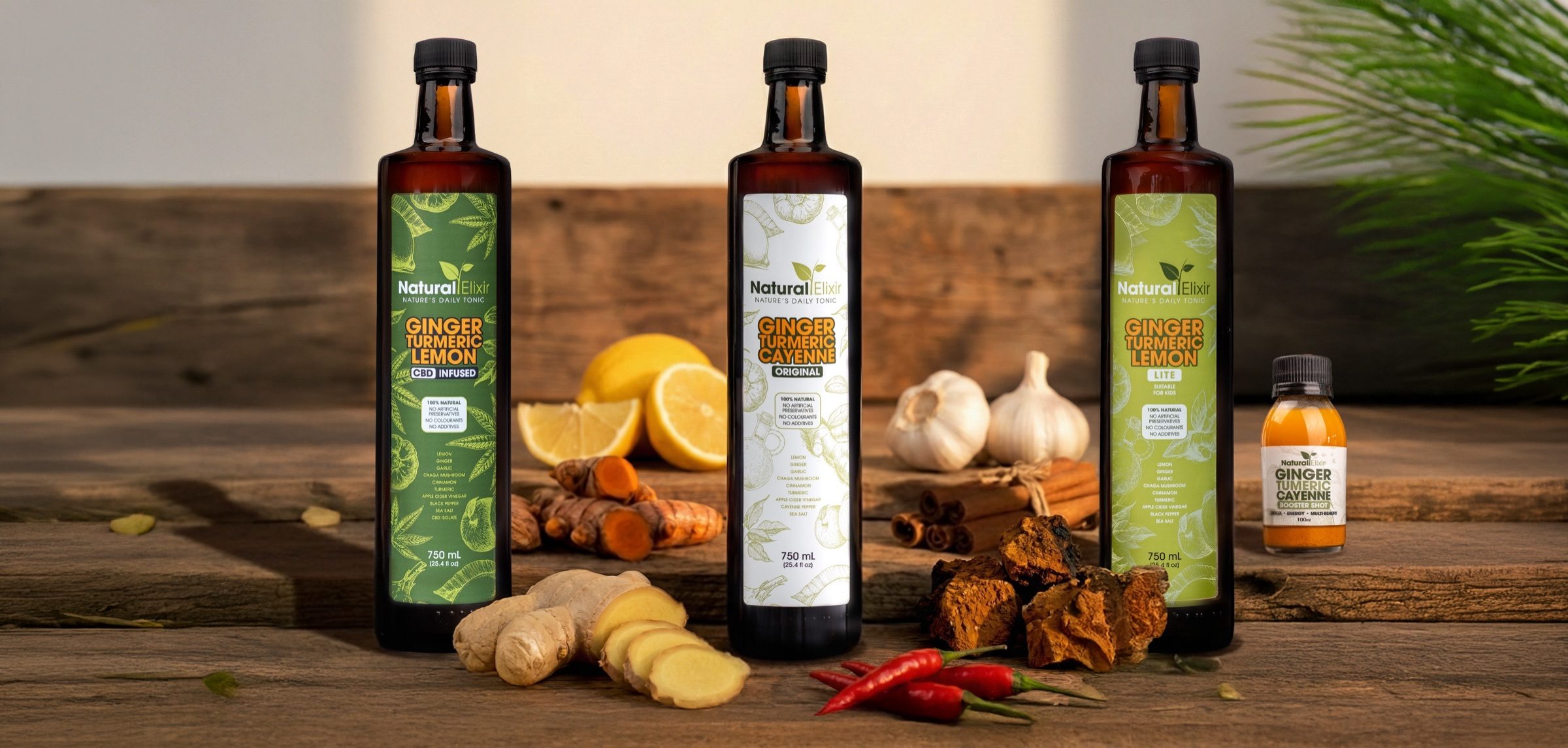 The three Natural Elixir 750 ml tonics and a 100 ml bottle on a wooden table with fresh ginger, turmeric, lemon, garlic, chillies, cinnamon and chaga