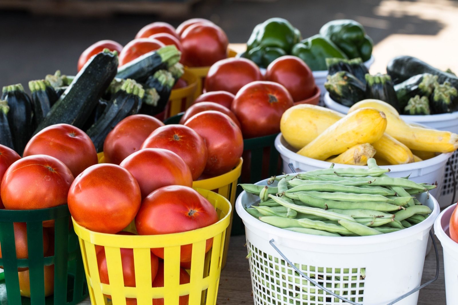 Baskets of tomatoes, beans, squash and peppers on a farmers market stall