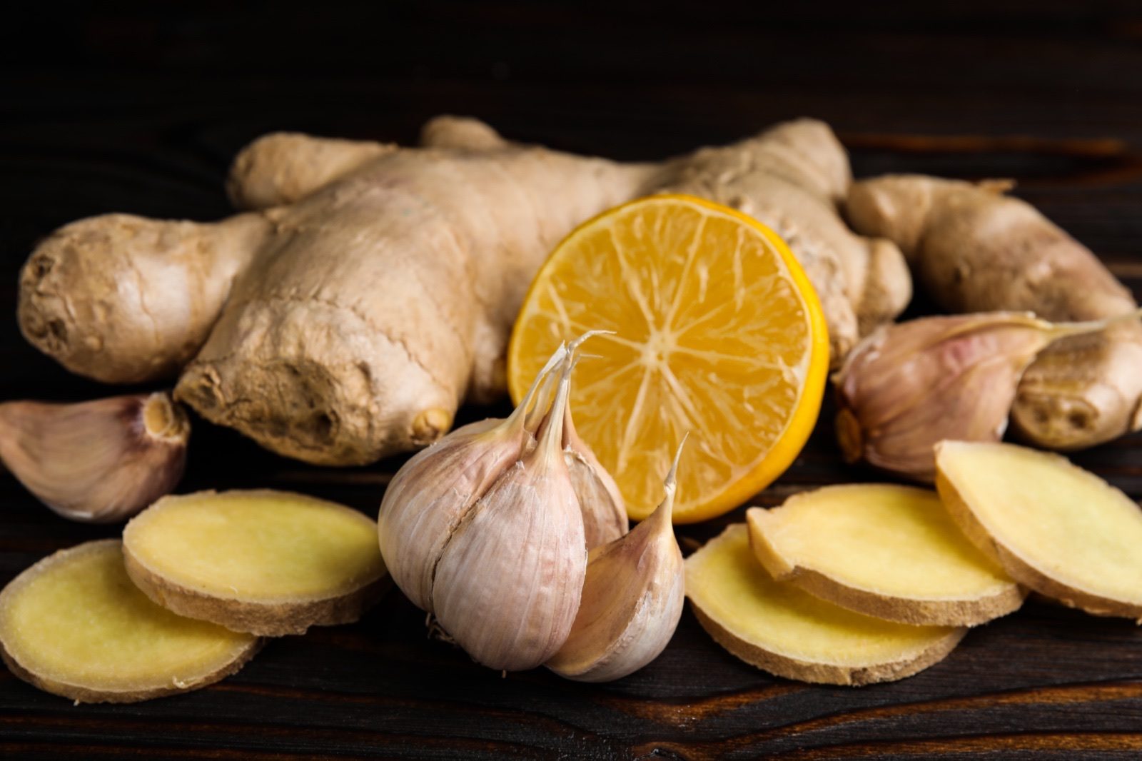 Fresh lemon, ginger root and garlic bulbs arranged on a dark surface