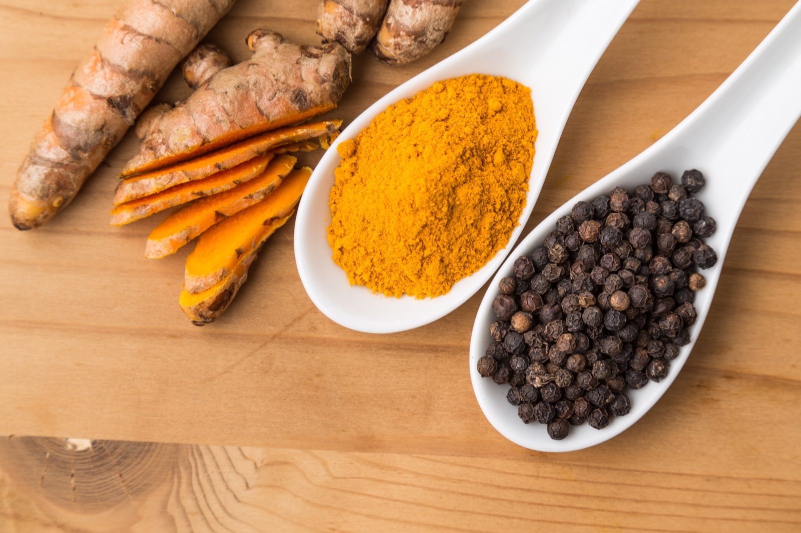 Fresh turmeric roots beside a spoon of black peppercorns