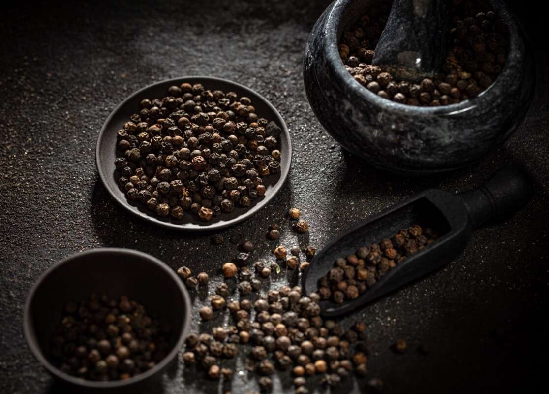Black peppercorns in dishes beside a mortar