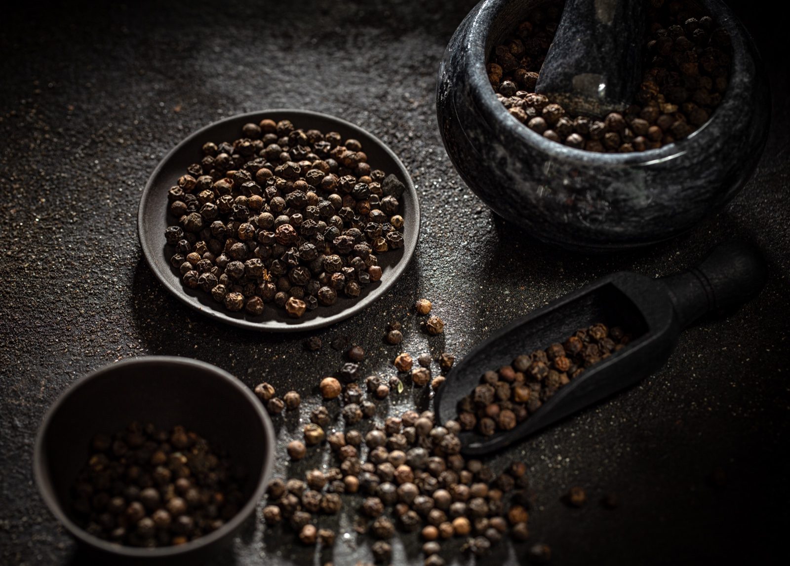 Black peppercorns in dishes with a mortar